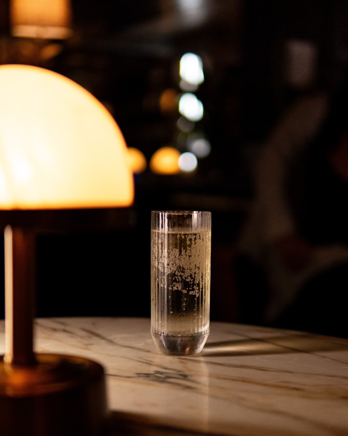 A tall highball beside a glowing alabaster table lamp