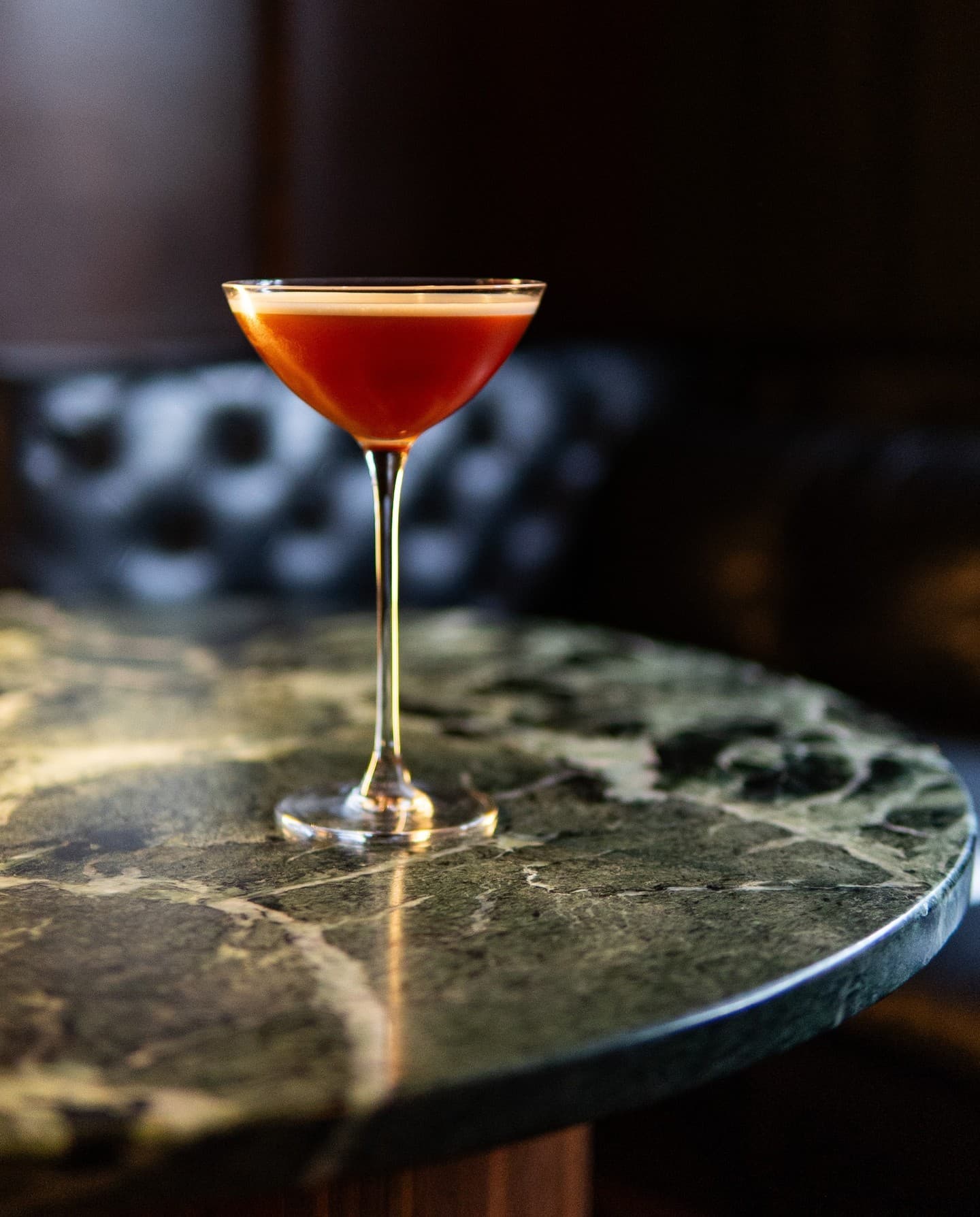 A ruby cocktail in a coupe on a green marble table