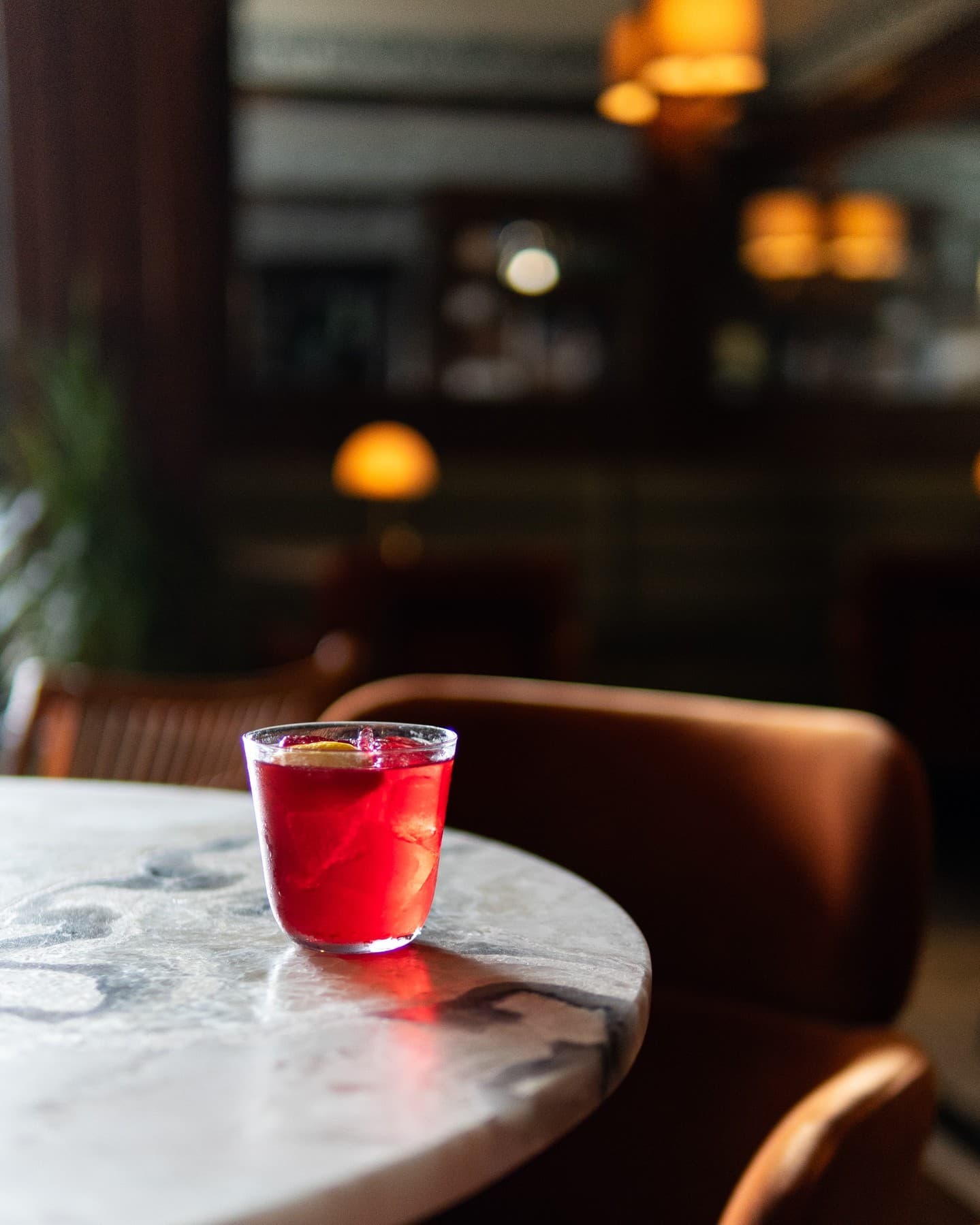 A deep red cocktail on white marble in low candlelight