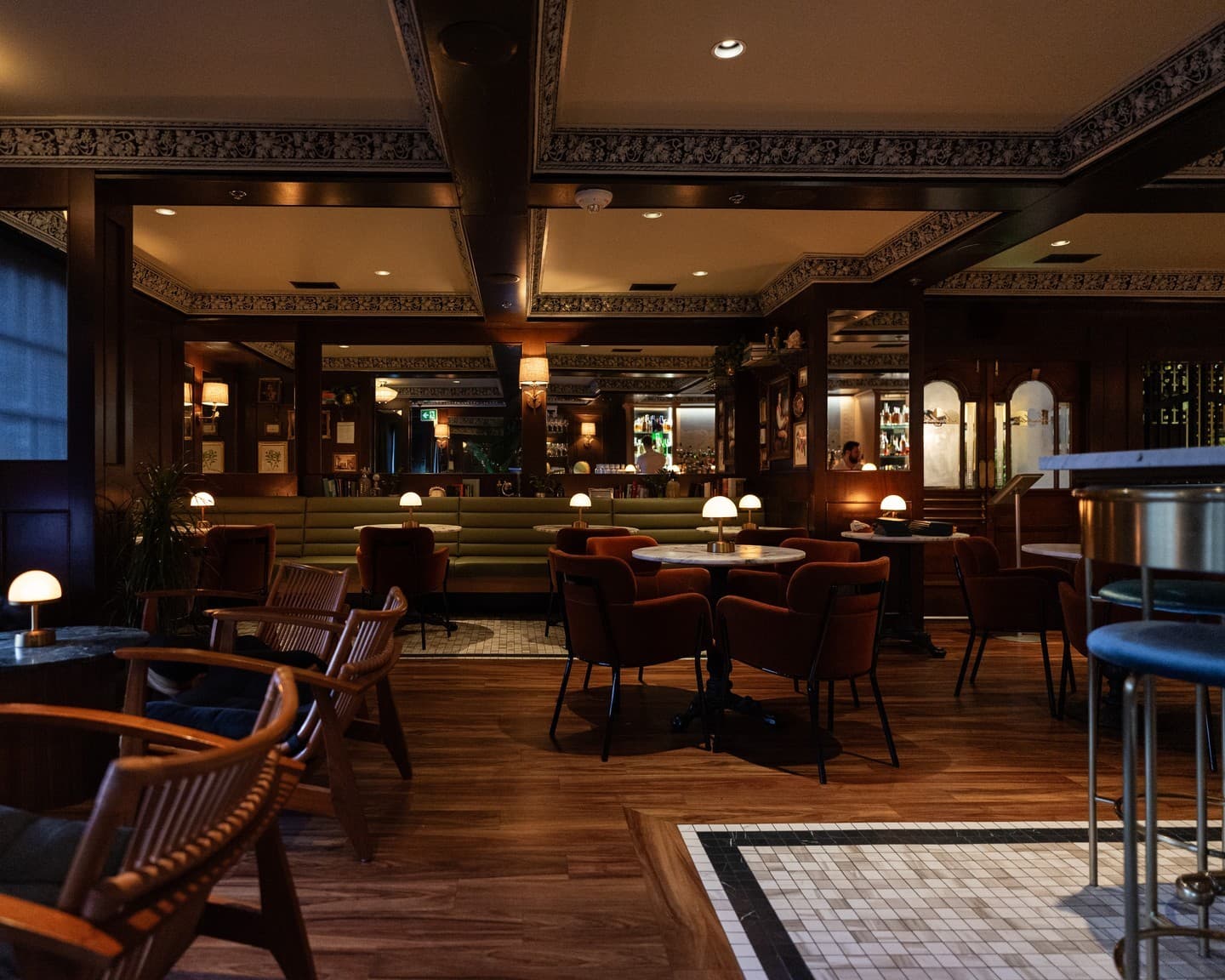 The full room at Humboldt Bar: green marble tables, leather chairs and an ornate pressed ceiling glowing in candlelight